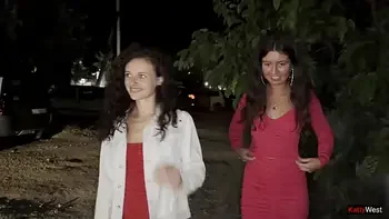 Two girlfriends pee together near a car in a public parking lot